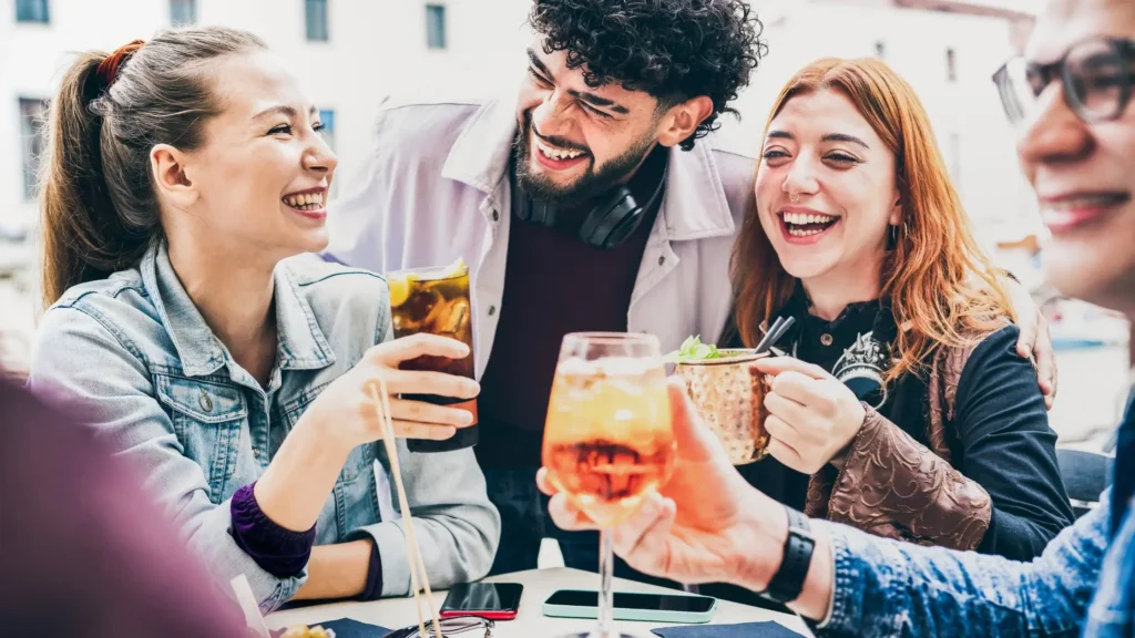 Grupa młodych dorosłych bawi się razem, trzymając drinki 0% i śmiejąc się w przyjaznej atmosferze