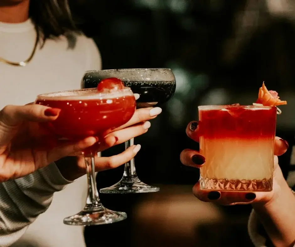 Trzy osoby wznoszące toast kolorowymi koktajlami – symbol wspólnego rytuału i wizualnej przyjemności smaku