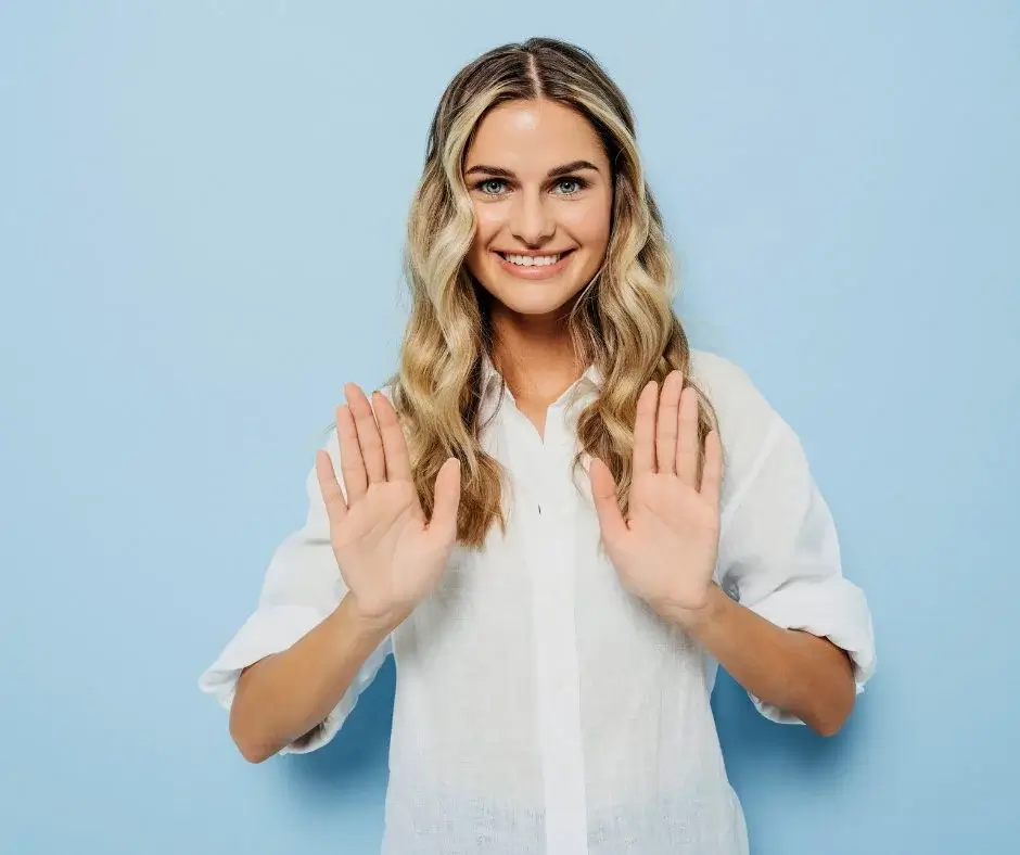Smiling woman raising her hands in a polite refusal gesture – calm and confident body language.