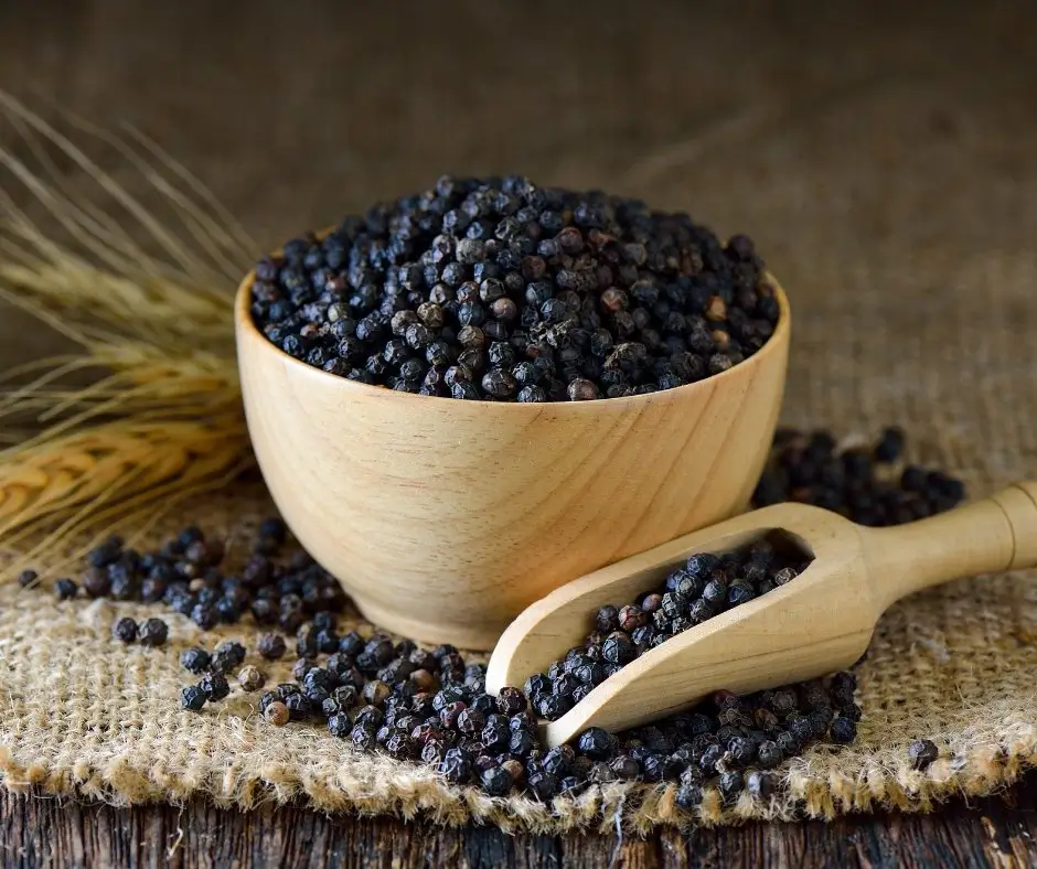 Ziarna czarnego pieprzu w drewnianej misce i łyżce na jutowym tle – naturalne źródło ostrości w bezalkoholowych destylatach.