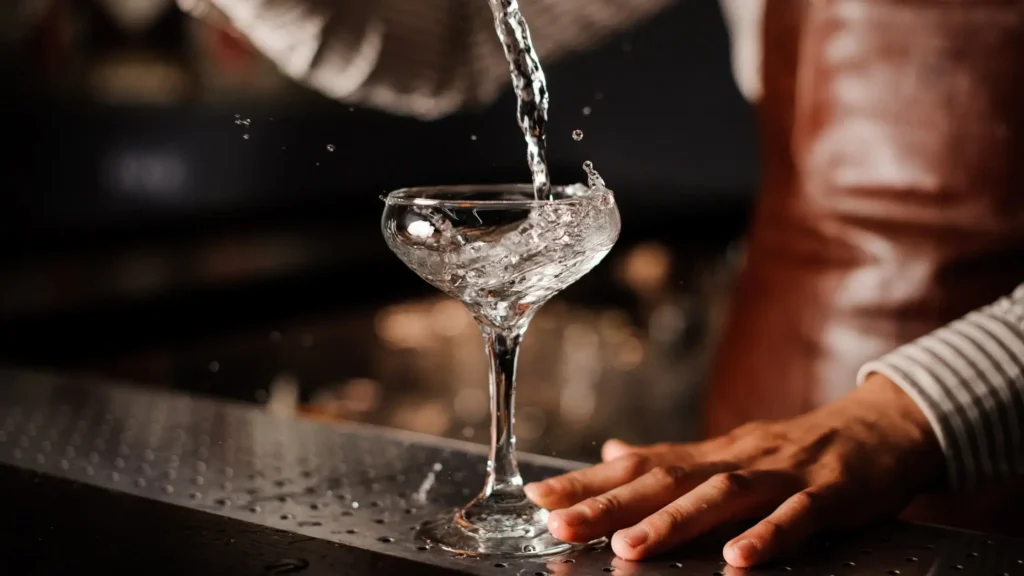 A bartender pours a clear, vodka-style 0% drink into a cocktail glass.
