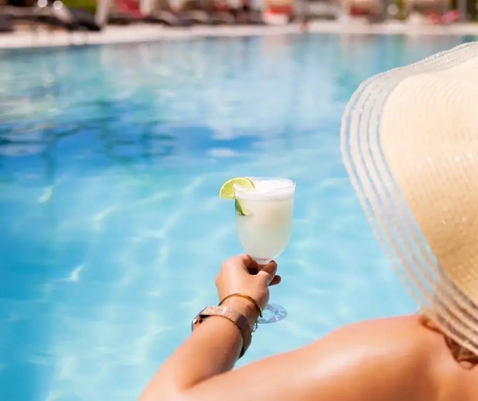 Person relaxing by the pool holding a non-alcoholic drink.