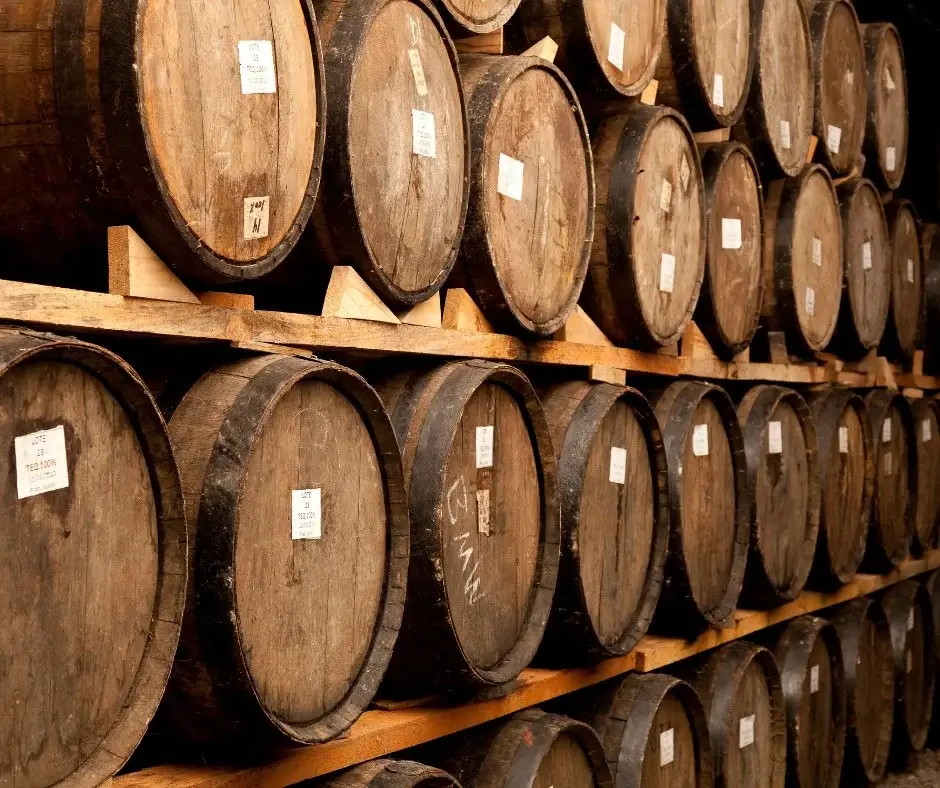 Rows of oak aging barrels stacked in a storage warehouse, viewed from the side.