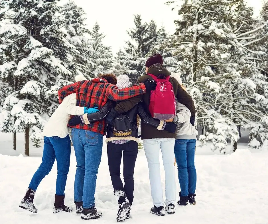 Gruppe von Menschen, die gemeinsam durch einen verschneiten Wald spazieren, winterliche Aktivität an der frischen Luft