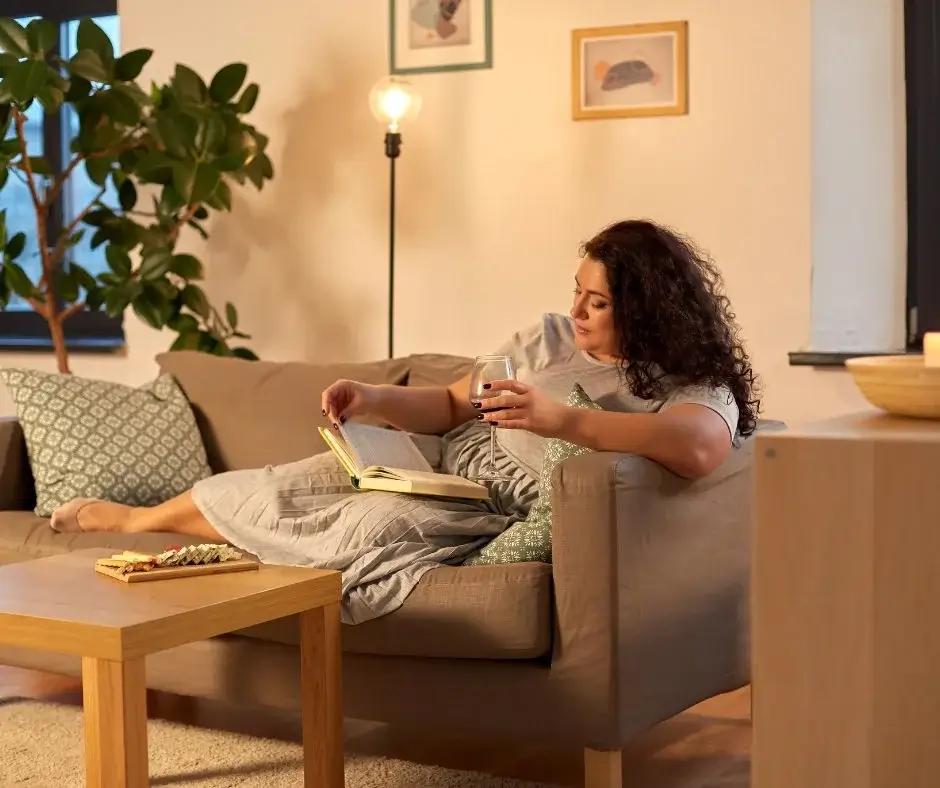 Person entspannt auf einem Sofa zu Hause, liest ein Buch und hält ein alkoholfreies Getränk, ruhiger Abend ohne Alkohol