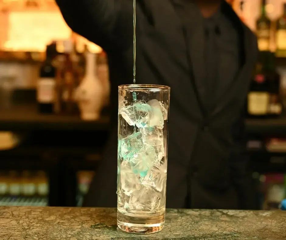 Zubereitung eines Zero-Proof-Cocktails an der Bar – Eingießen einer Zutat über Eis als Teil des Trinkrituals